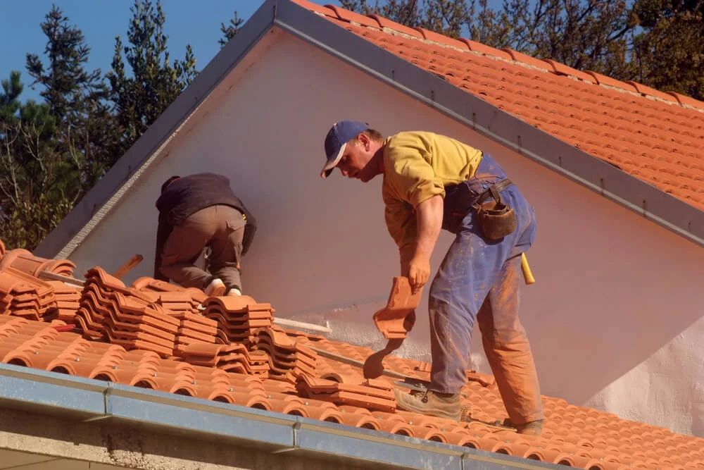 Two men repairing a roof in San Antonio, working together with a brick for the roofing project.
