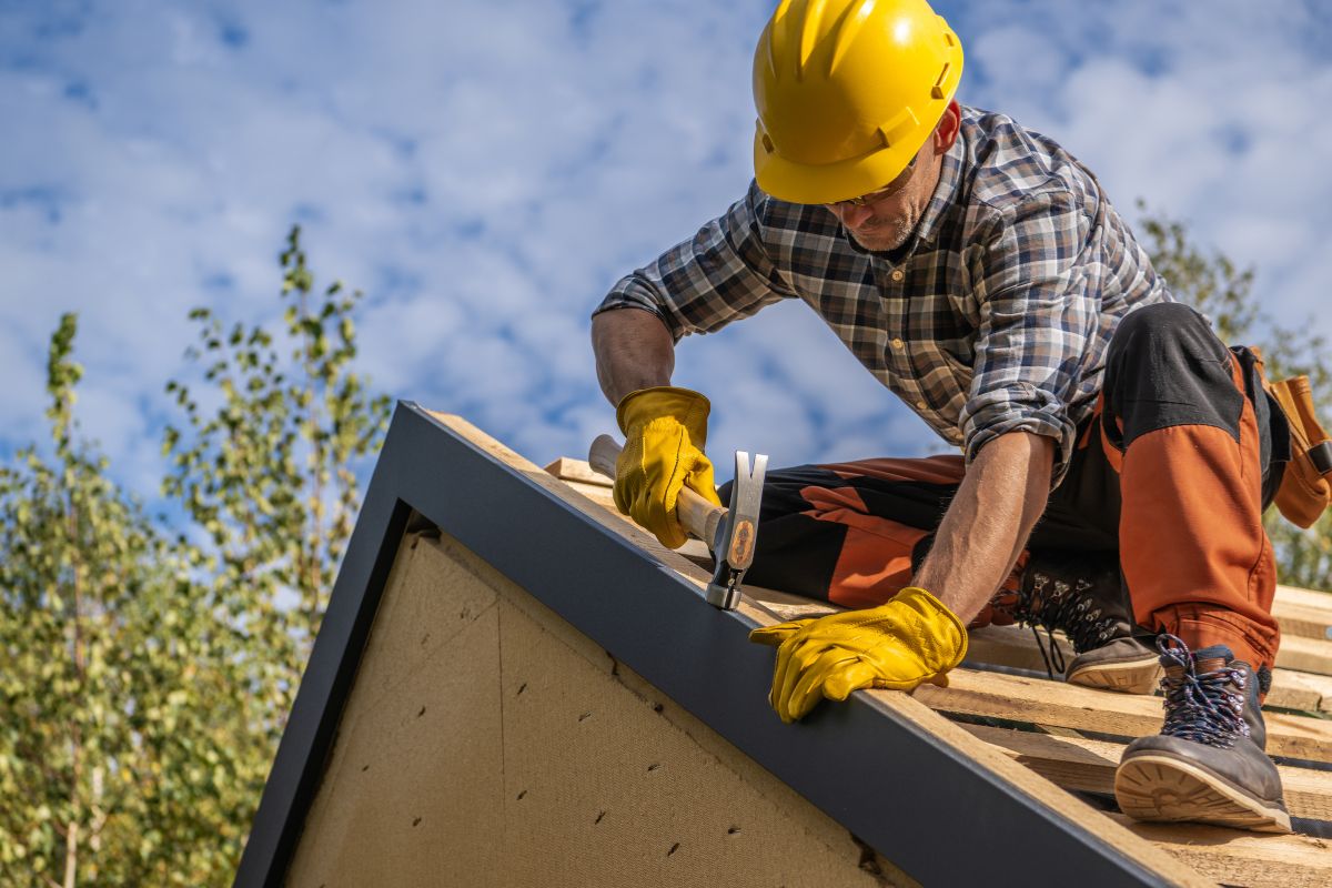 A man wearing a hard hat and yellow safety vest is actively working on a roof, ensuring safety and construction progress.