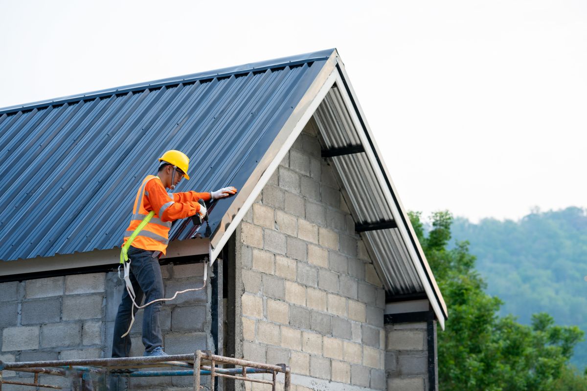 A man wearing an orange vest and hard hat is actively working on the construction of a house.